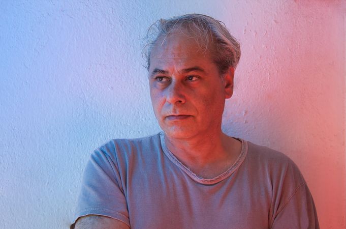 Portrait of serious middle aged man in gray shirt looking away against light background in UV lit studio