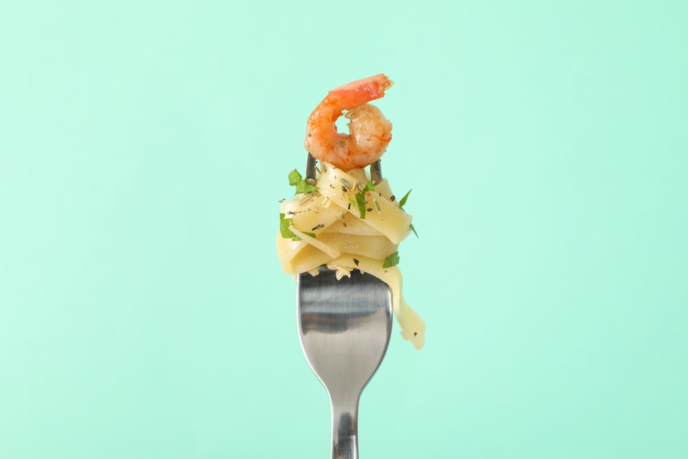 Fork with tasty pasta on mint background, close up