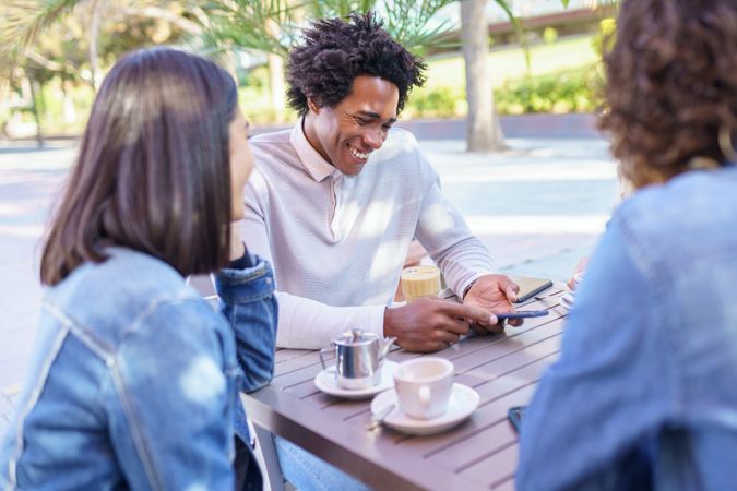 Multi-ethnic friends smiling and laughing at joke over coffee and juice at outside table