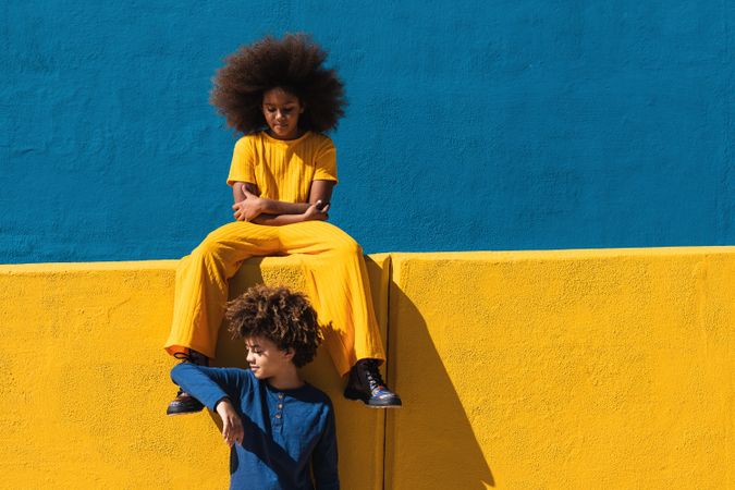 Black curly haired girl and boy resting near colorful wall