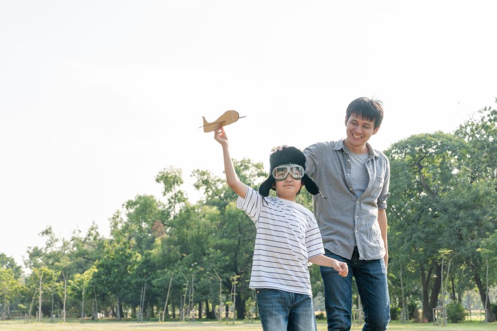 Father and son playing with toy plane in park on overcast day