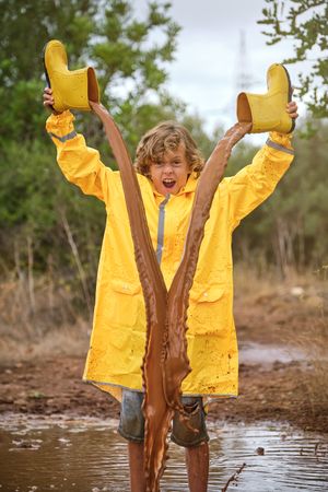 Excited boy pouring dirty water out of gumboots