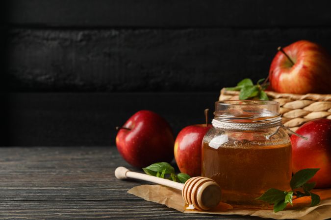 Pot of honey with dipper in front of basket of apples with copy space