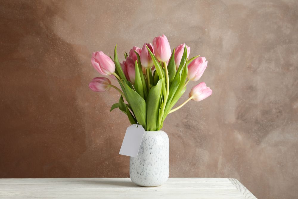 Vase with tulips on wooden table, space for text