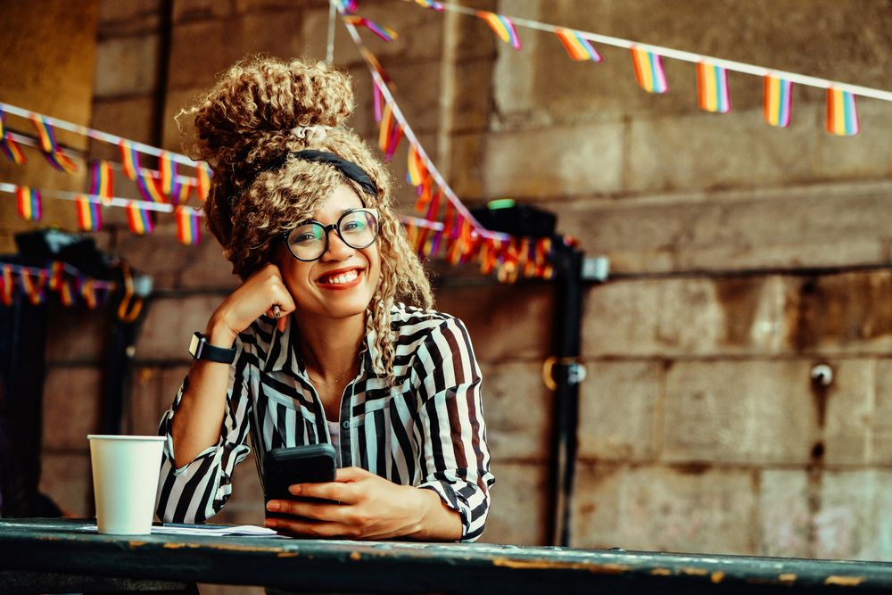 Happy Black woman in stripe shirt texting in cafe, space for text