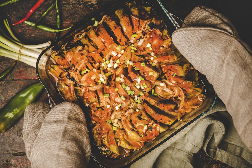 Grey oven mitts holding a roasted squash casserole against wooden surface