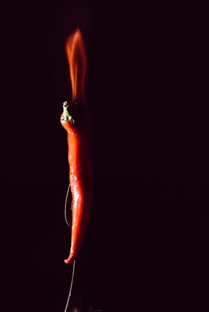 red chili pepper on fire in fork on a dark background
