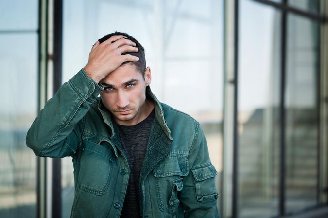 Male in green jacket looking into camera as he runs his hand through his hair