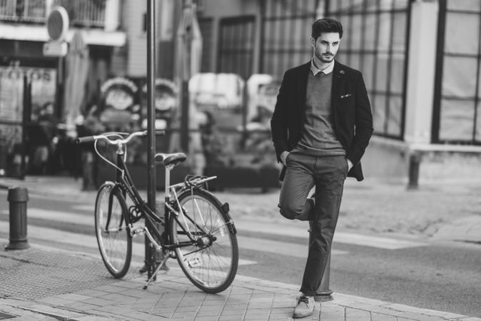 B&W shot of man standing on the street wearing elegant suit next to parked vintage bicycle