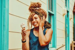 Entertained Black female snacking on an ice cream cone in the sun