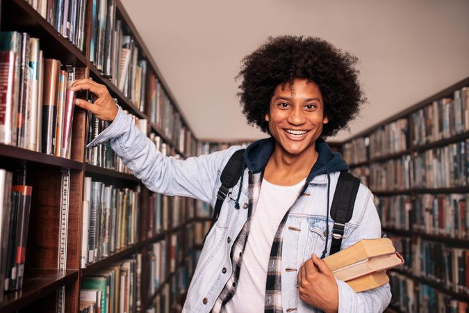 Smiling young man taking book from bookshelf