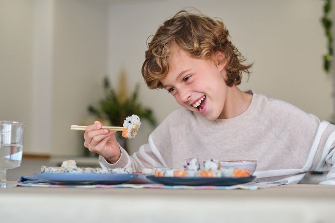 Cheerful boy eating sushi at home