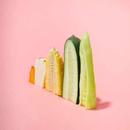 Various vegetables sliced in half showing cross-section on pastel pink background