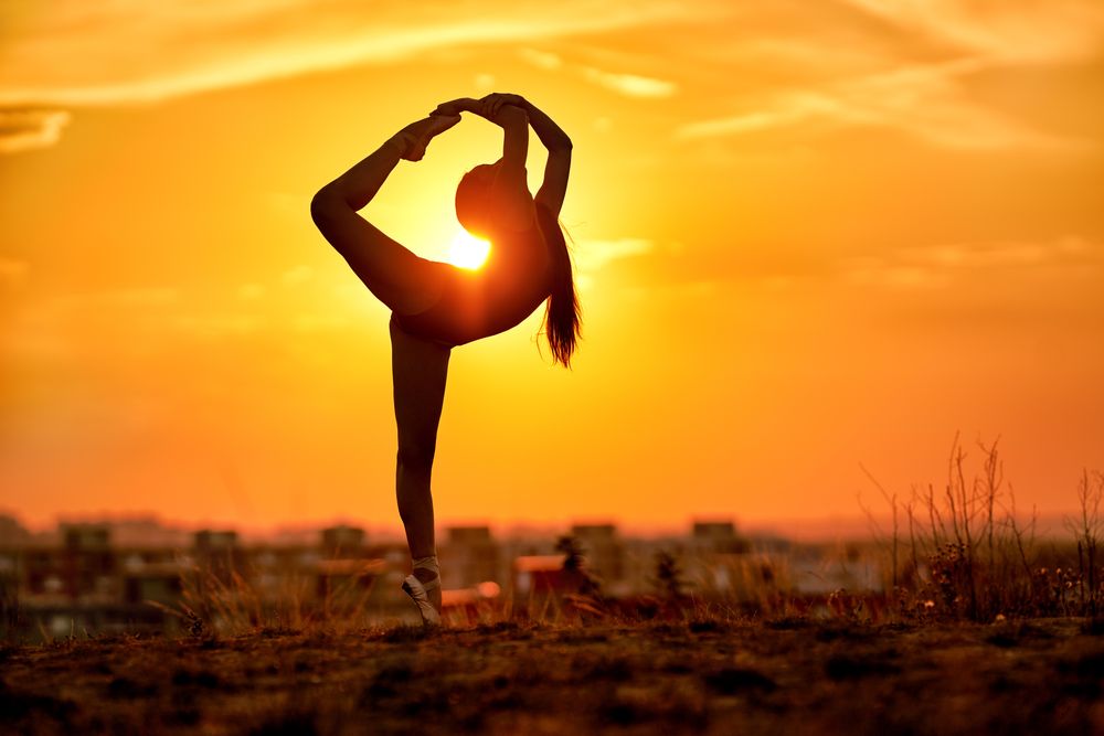 Silhouette of girl doing dancer pose during sunset