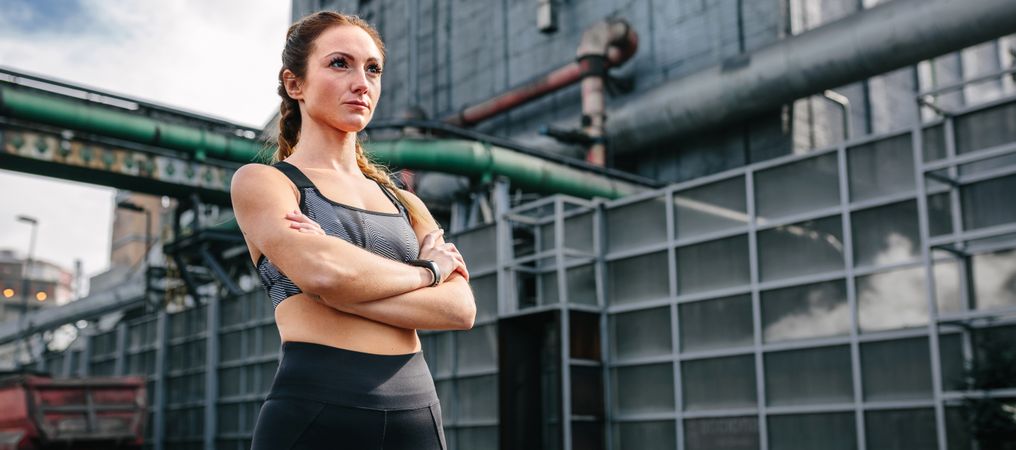 Sportswoman with crossed arms posing in front of a factory