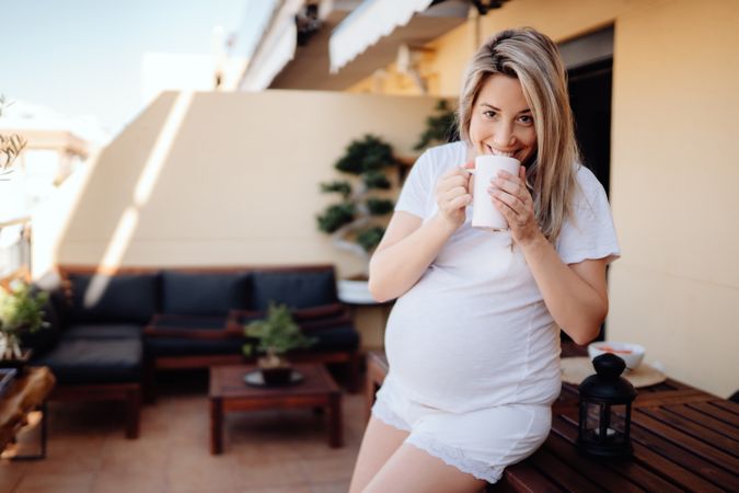 Smiling pregnant woman having drink at terrace