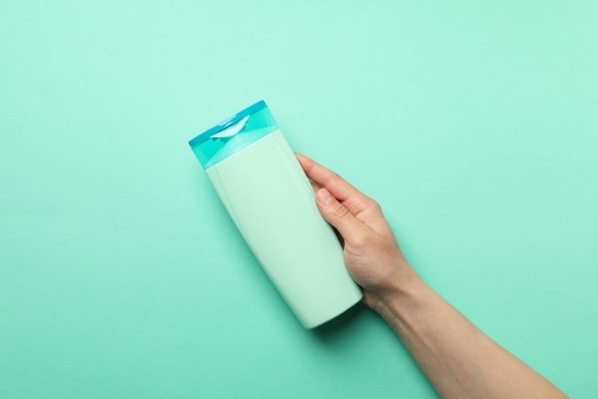 Female hand holds shampoo bottle on mint background, space for text