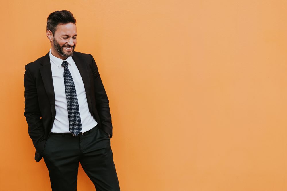 Adult stylish man in costume near orange wall