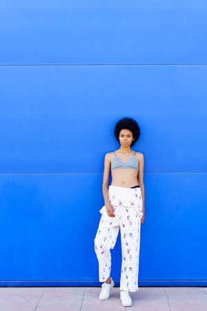 Woman in floral coveralls looking away while leaning against blue outdoor wall