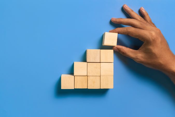 male hand put stairway wooden blocks isolated on blue background