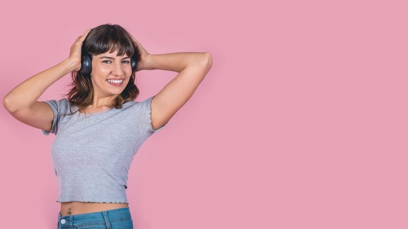 Happy woman in headphones listening to music isolated on pink background. Studio shot. Copy space
