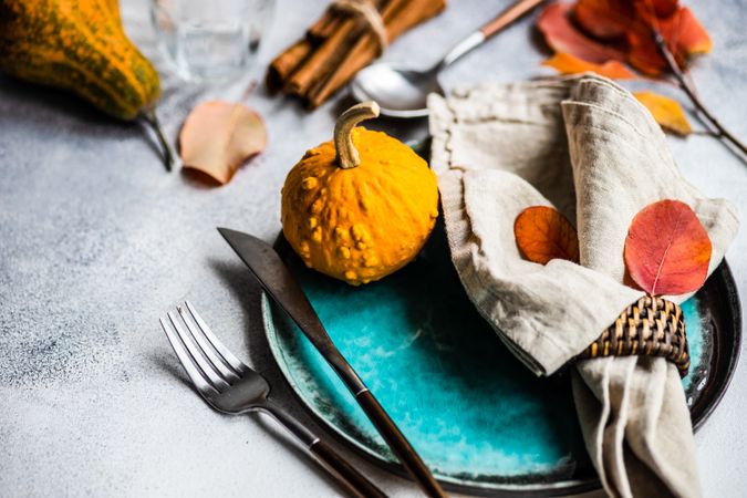 Autumn place setting with colorful leaves, gourd and cinnamon sticks garnishing teal plate