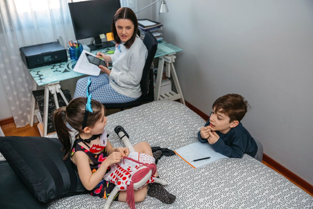 Children playing and doing homework talking with their mother who works at home