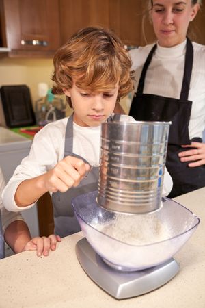 Little boy adding flour to bowl for batter