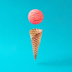 Waffle cone with separated scoop of pink ice cream on bright blue background