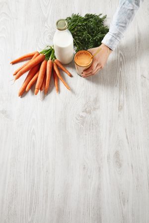 Top view of man reaching for carrot juice with bunch of carrots and bottle of milk with copy space