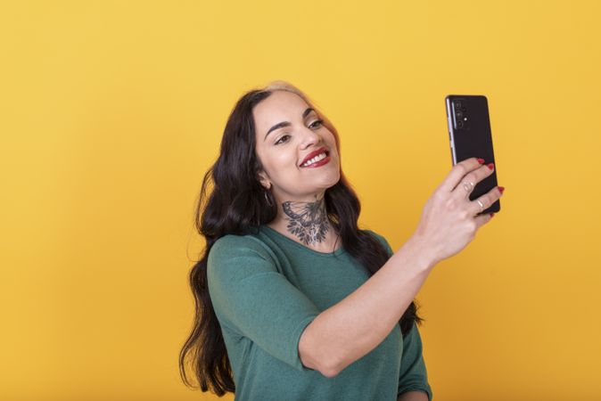 Portrait of a woman making a selfie over yellow background. Studio shot.