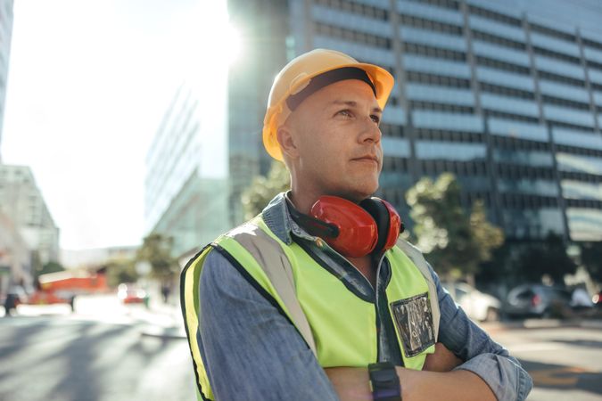 Construction worker looking away thoughtfully in the city in safety gear