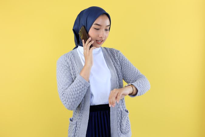 Young Asian Woman with Blue Hijab Talking at the Phone While Looking at Her Watch
