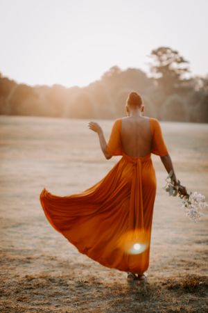 Back view of woman in an orange dress holding light flowers at sunrise