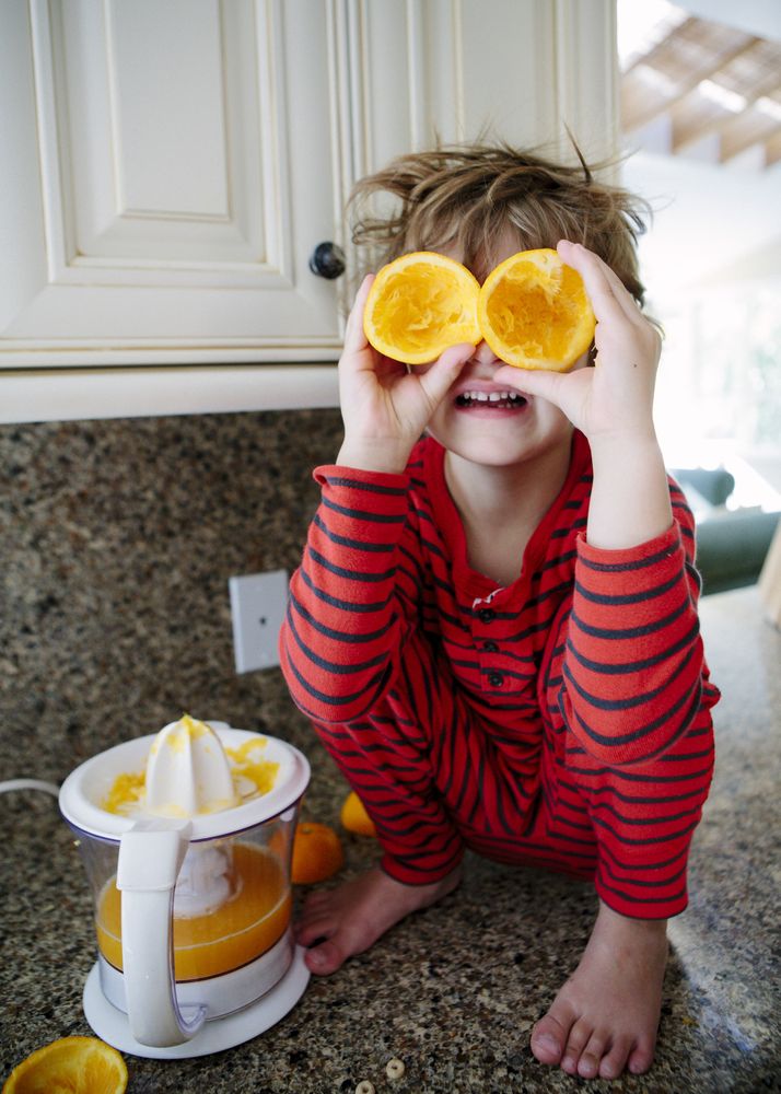 Boy's wearing red striped pajama holding a squeezed orange in kitchen