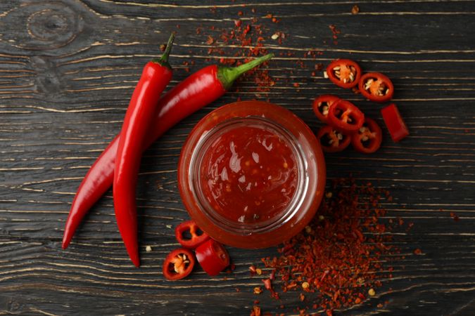 Chilli pepper and glass jar of sauce on wooden  background, top view