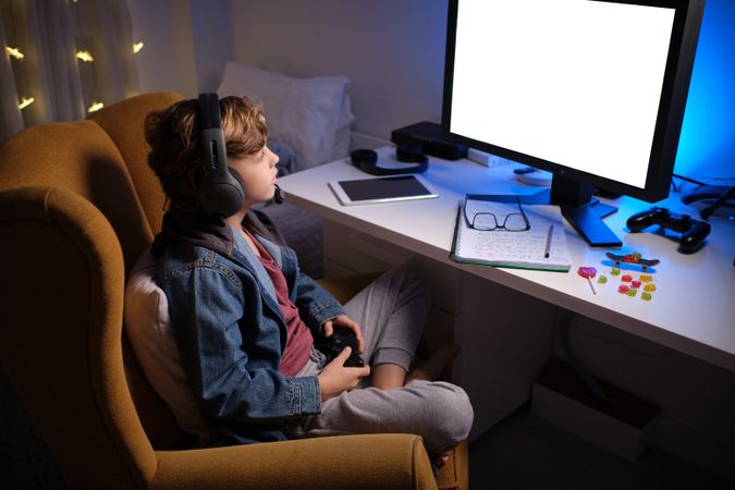 Kid in headphones using computer for game in dark room