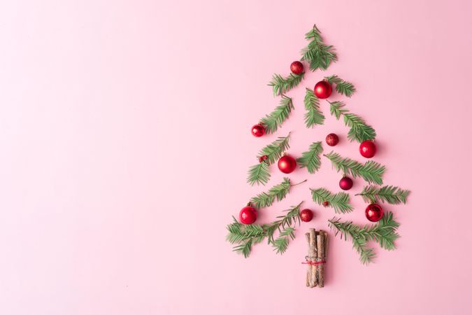 Christmas tree made with evergreen fir, bauble decoration and cinnamon sticks on pink background