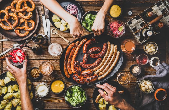 German sausages and pretzels displayed on wooden table with hands cutting sausage