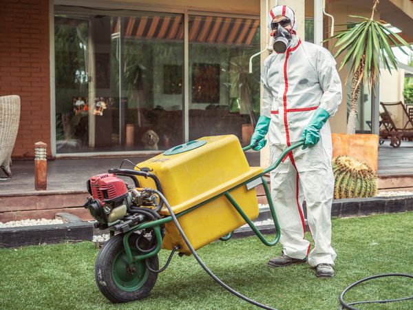 Specialist in uniform for fumigation holding yellow trolley in yard