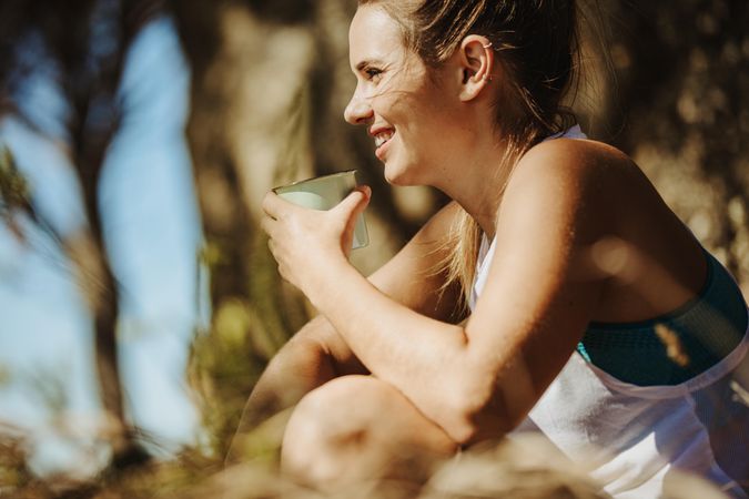 Smiling young woman drinking coffee while trekking
