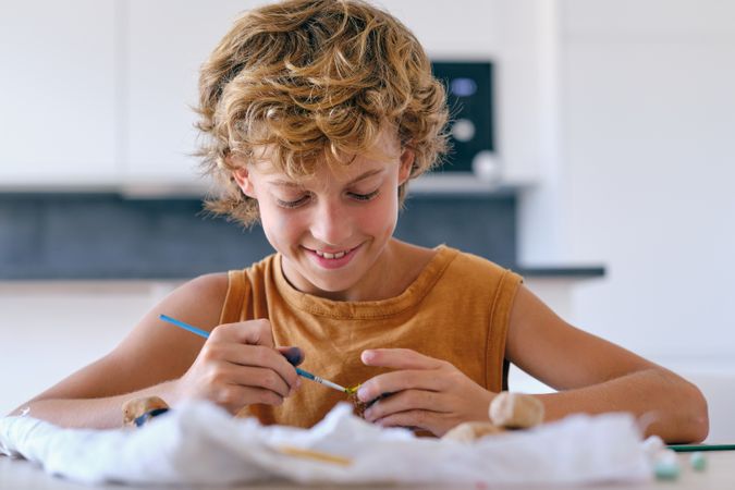 Smiling boy painting pebble with gouache