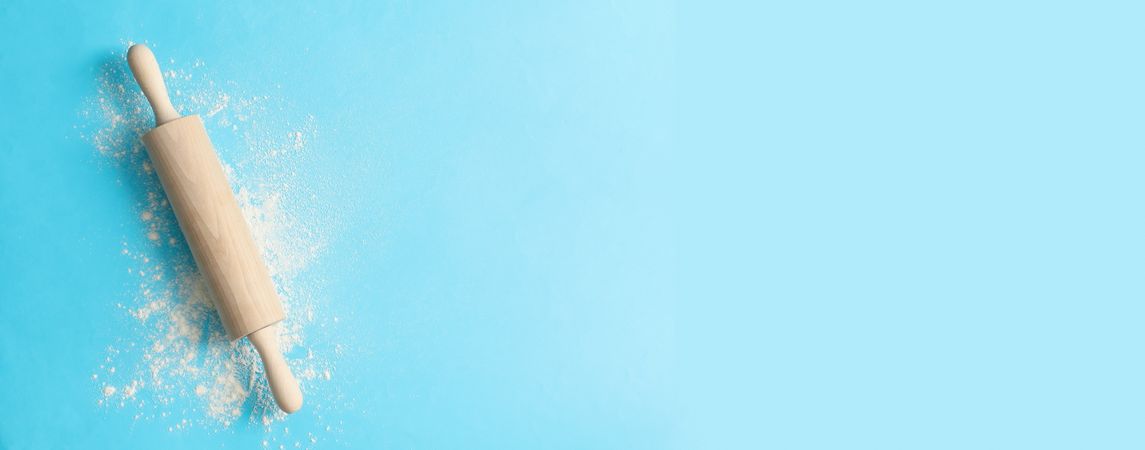 Rolling pin and flour on blue background