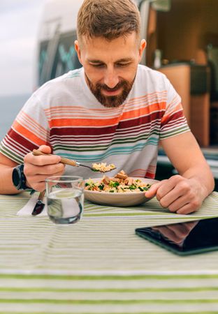 White male eating vegetable dish on outdoor table, vertical