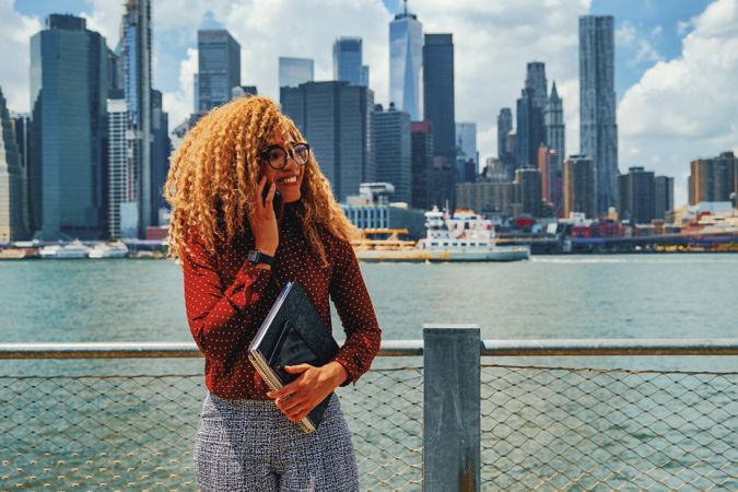 Happy professional Black female taking phone call by Hudson River