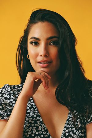 Surprised Hispanic woman wearing dress standing in yellow room, vertical