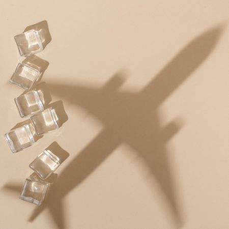 Flat lay of ice cubes on beige background with shadow of airplane