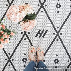 Aerial view of person wearing pink floral sneakers standing beside pink floral arrangement on patterned tiles 0J69N0