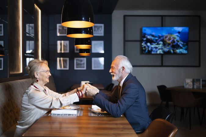 Mature couple smiling and holding hands over restaurant table