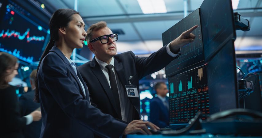 Team of Two Multiethnic Stock Exchange Brokers Using Computer, Chatting About the Asset Management Strategy for International Business Client, Working in an Office Building with Computer Screens